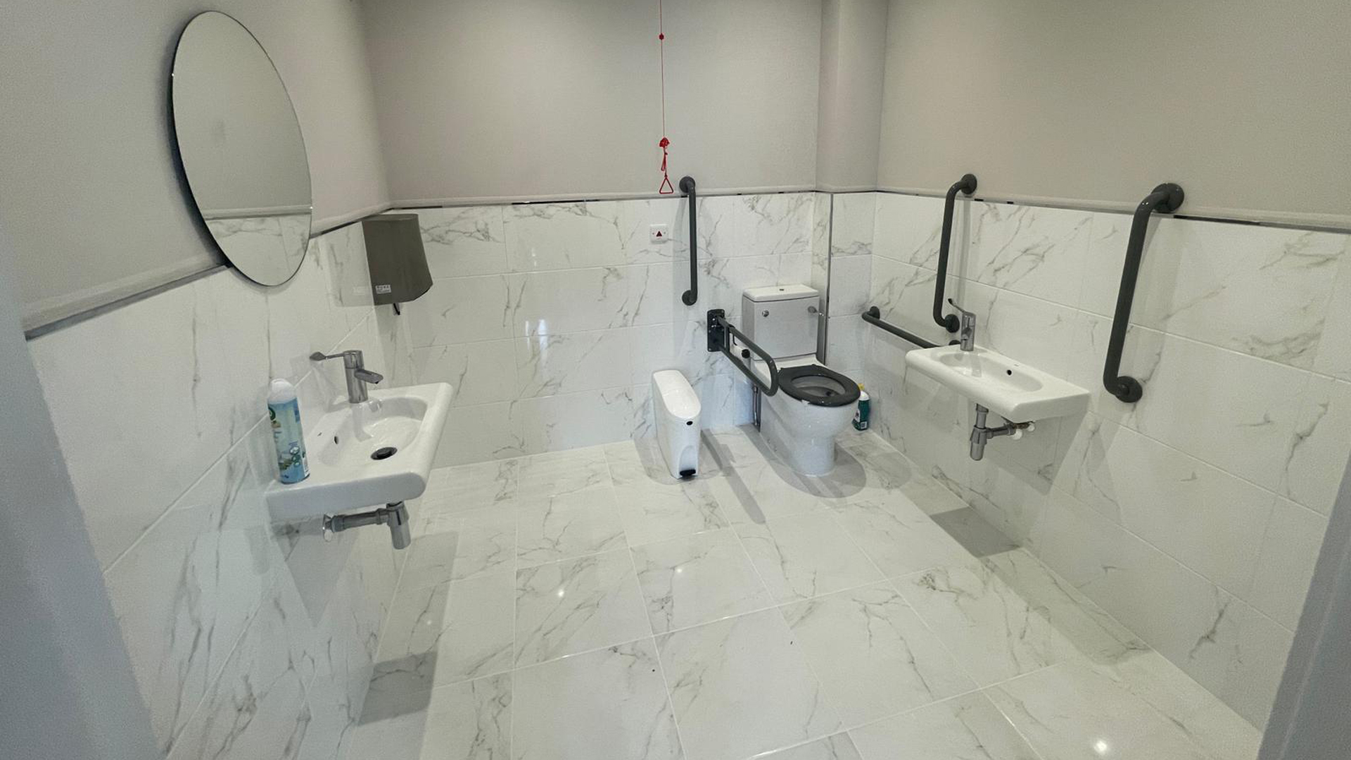 WC with toilet and two sinks, plus mirror and grab rails. White marbled tiling