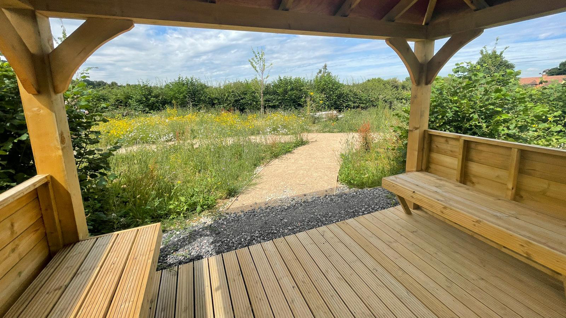 wooden gazebo seating area surrounded by wildflower and winding path