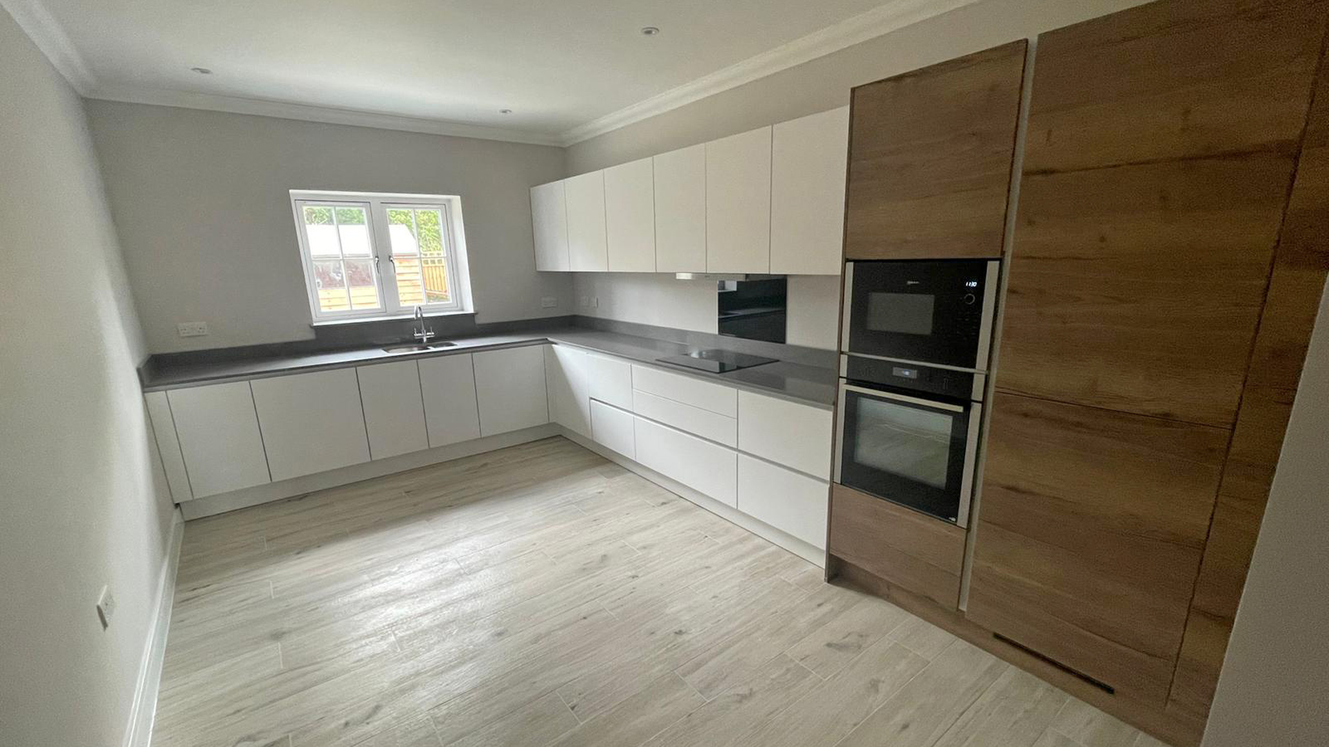 New build kitchen with grey worktops, white cabinets and dark wood tall housing
