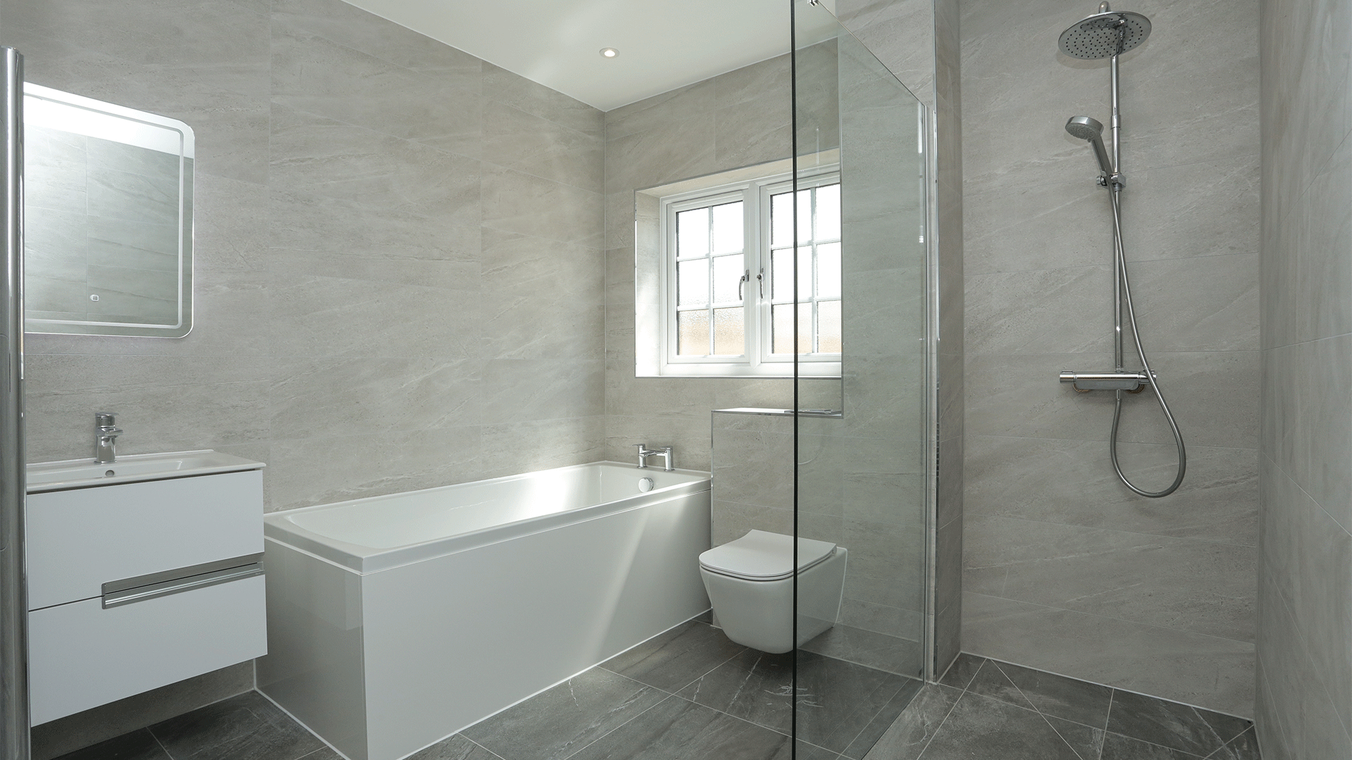 Grey tiled bathroom with shower, toilet, bath and sink basin with mirror at Miller's Meadow