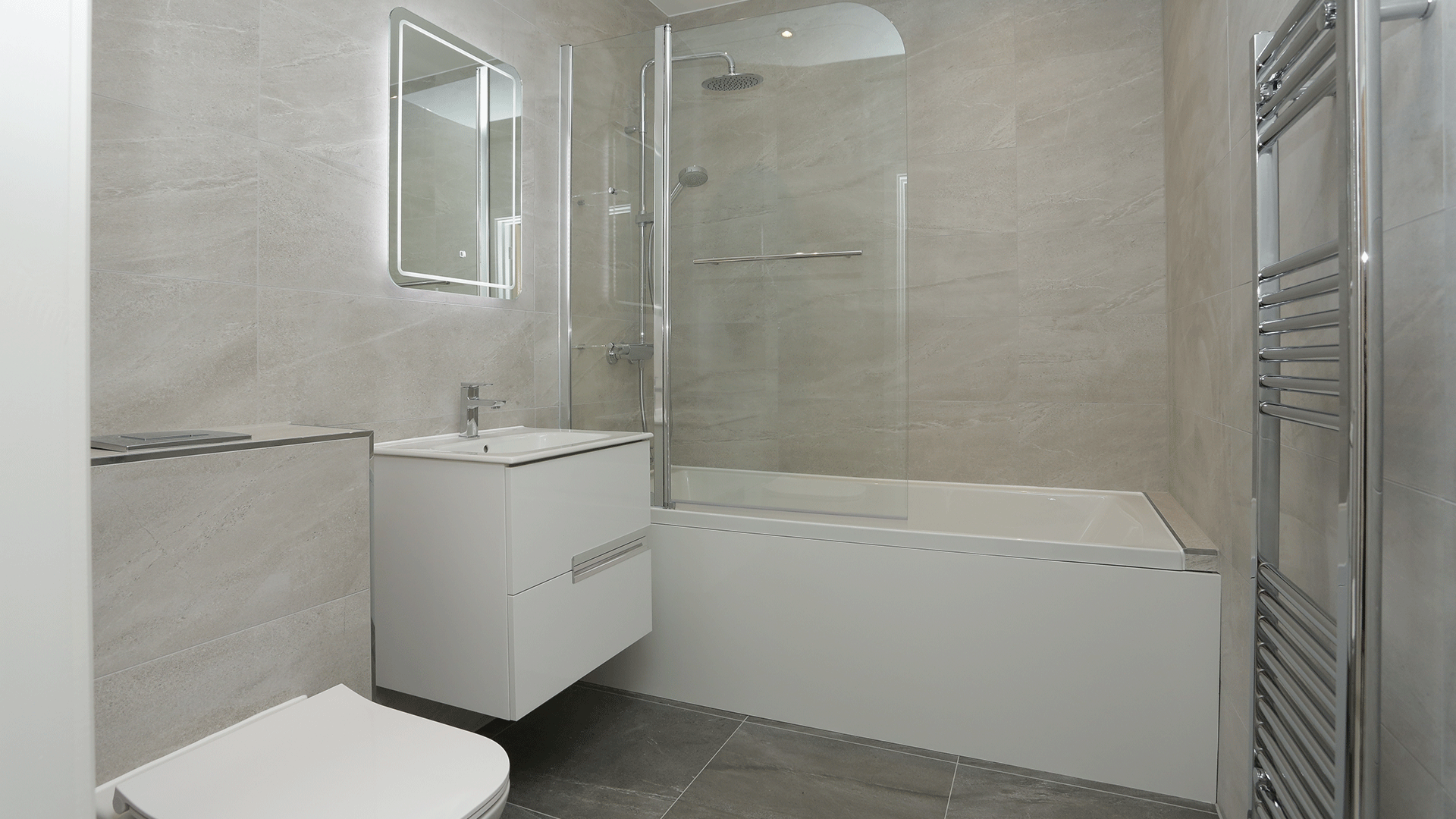 Tiled bathroom with bath shower and shower screen, toilet, and sink basin with mirror at Miller's Meadow