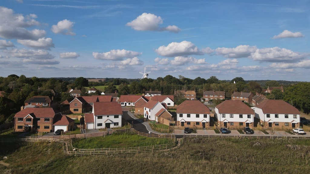 Aerial shot of Miller's Meadow new build housing development situated in front of a white windmill and surrounded by green fields