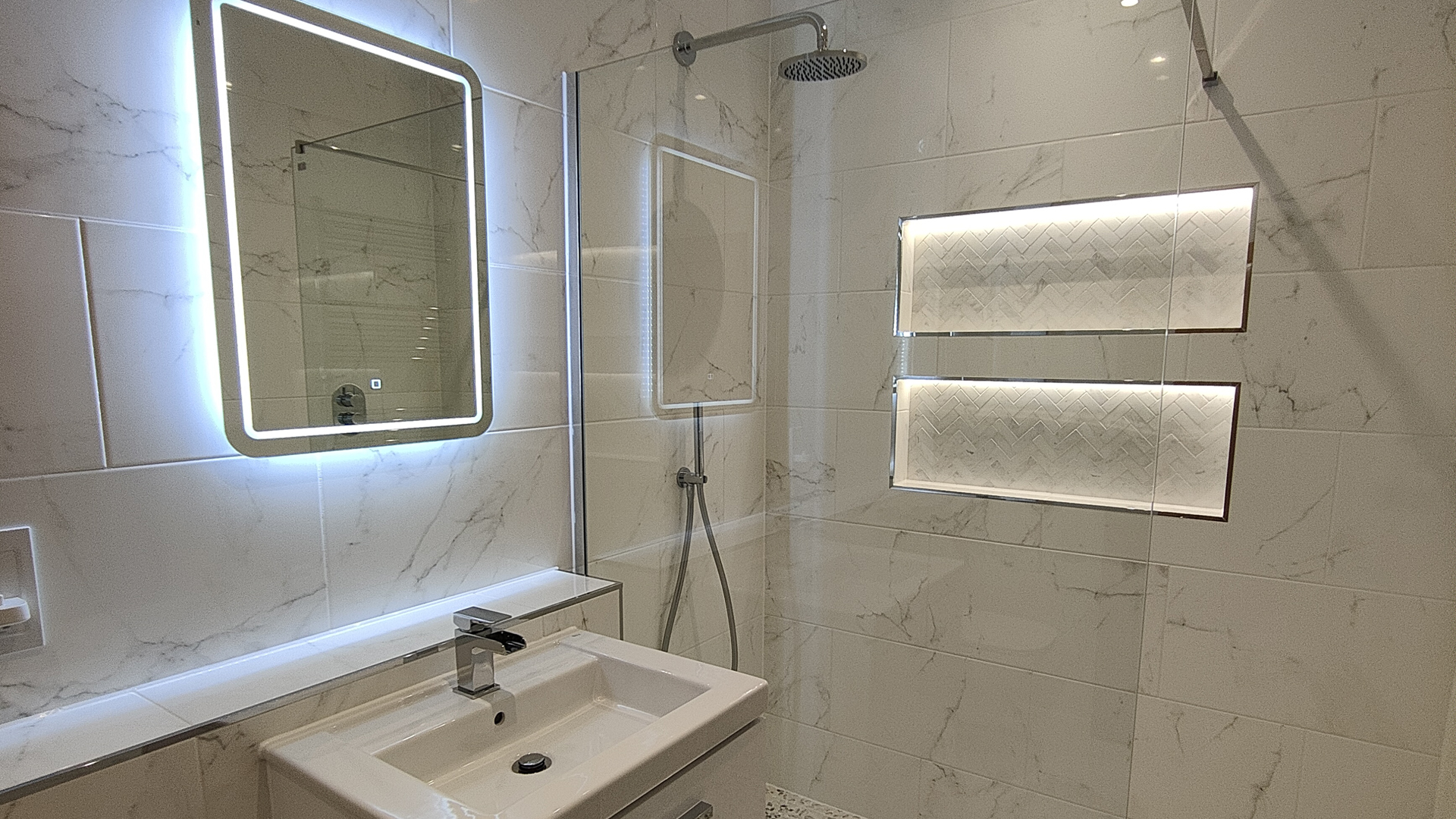 Marble tiled bathroom with light up mirror and recessed shelves in shower wall