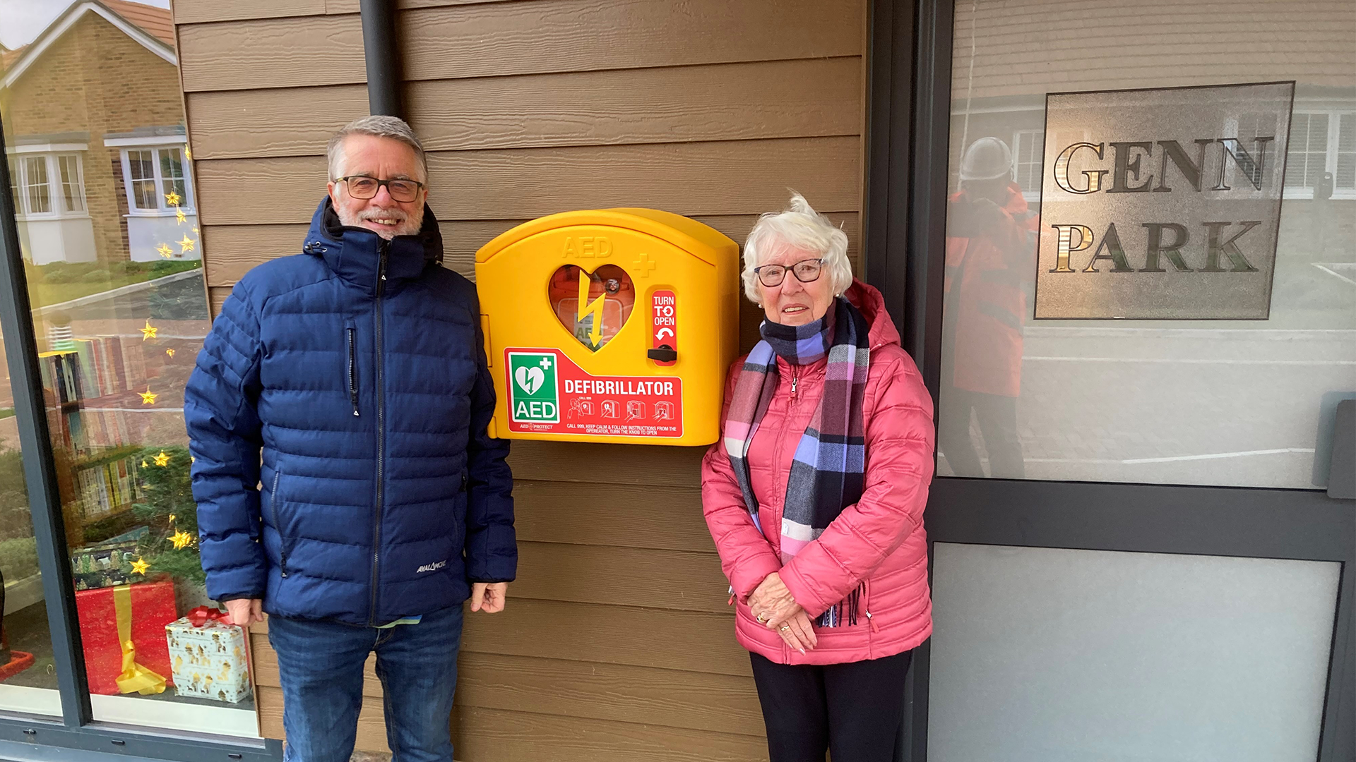 two cobnut park residents stand next to a bright yellow box housing a defibrillator