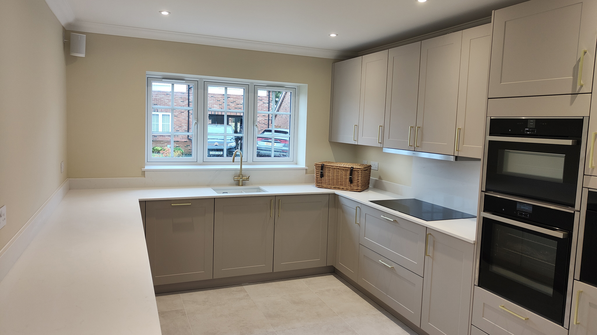 grey shaker kitchen with high level oven and large window above the sink