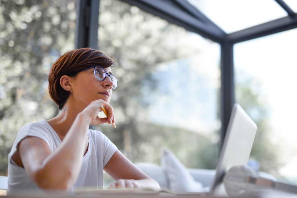 Woman thinking at desk in a light room with windows