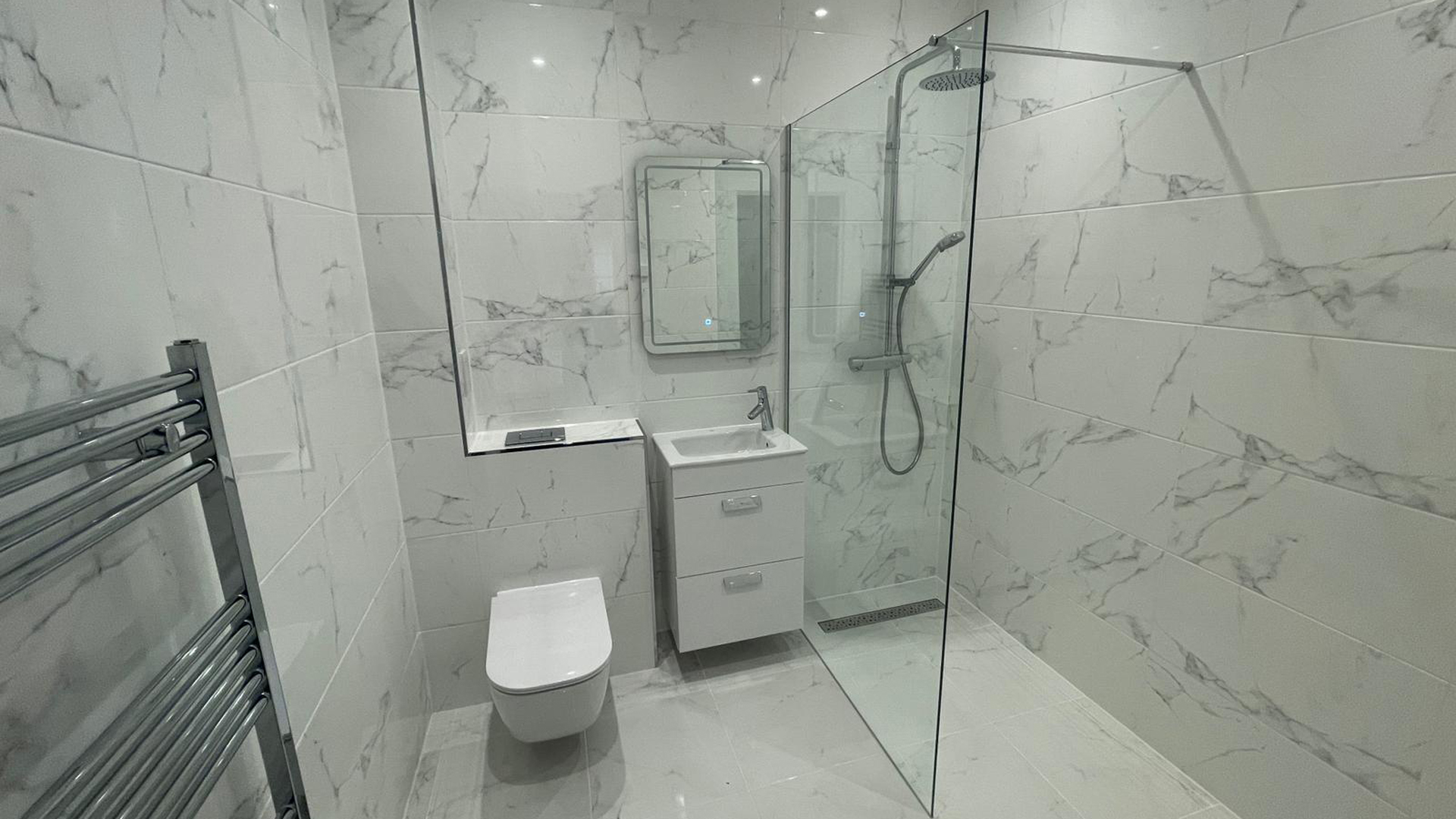 Shower room with white marbled tiles, mirror and chrome towel rail