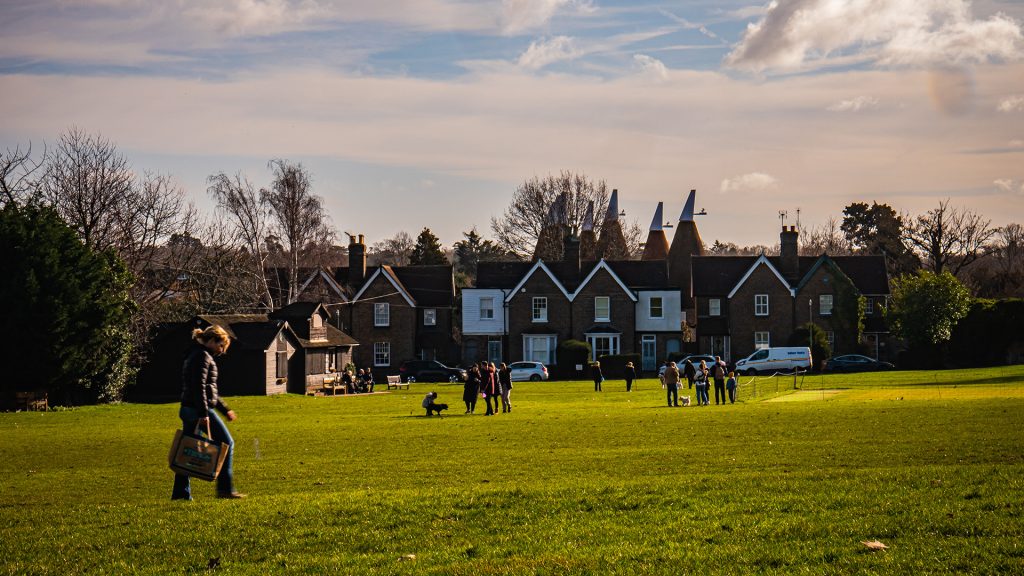 people walking across a green fields on a cold day, the sun is shining, there are dogs and families