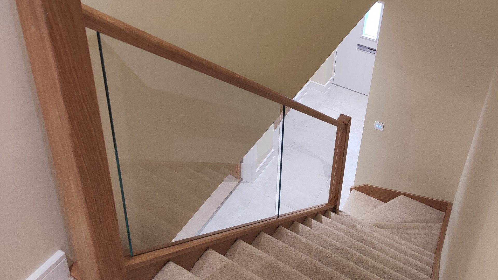 oak stair handrail with glass railing and carpeted stairs