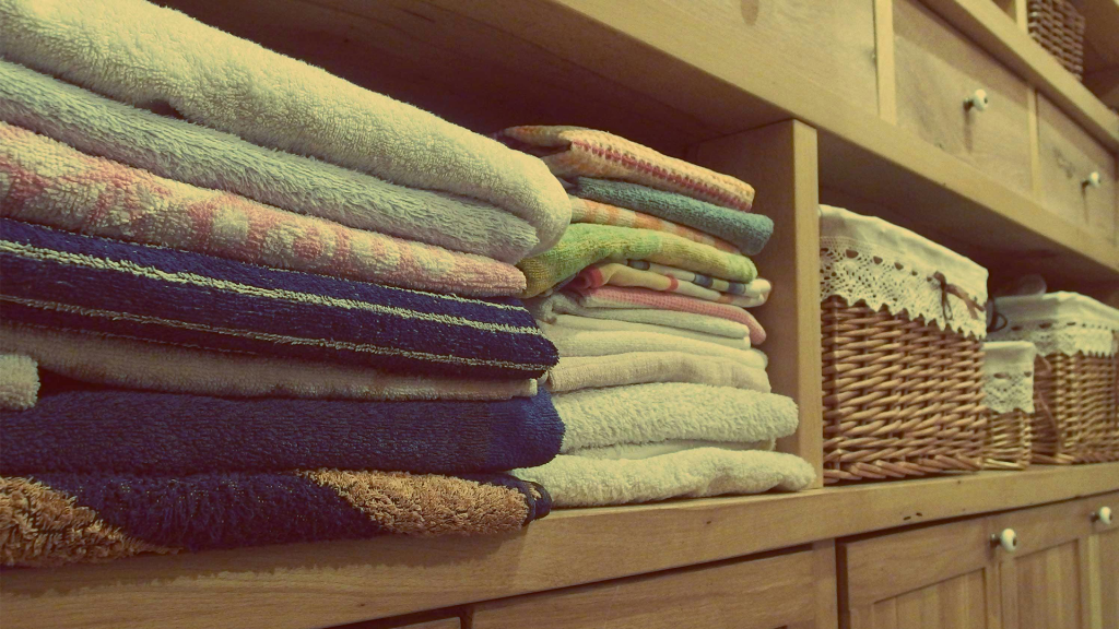 A low angle show of a laundry cupboard, several colourful folded towels are in the shelf closets to the camera, next to this shelf is some basket storage