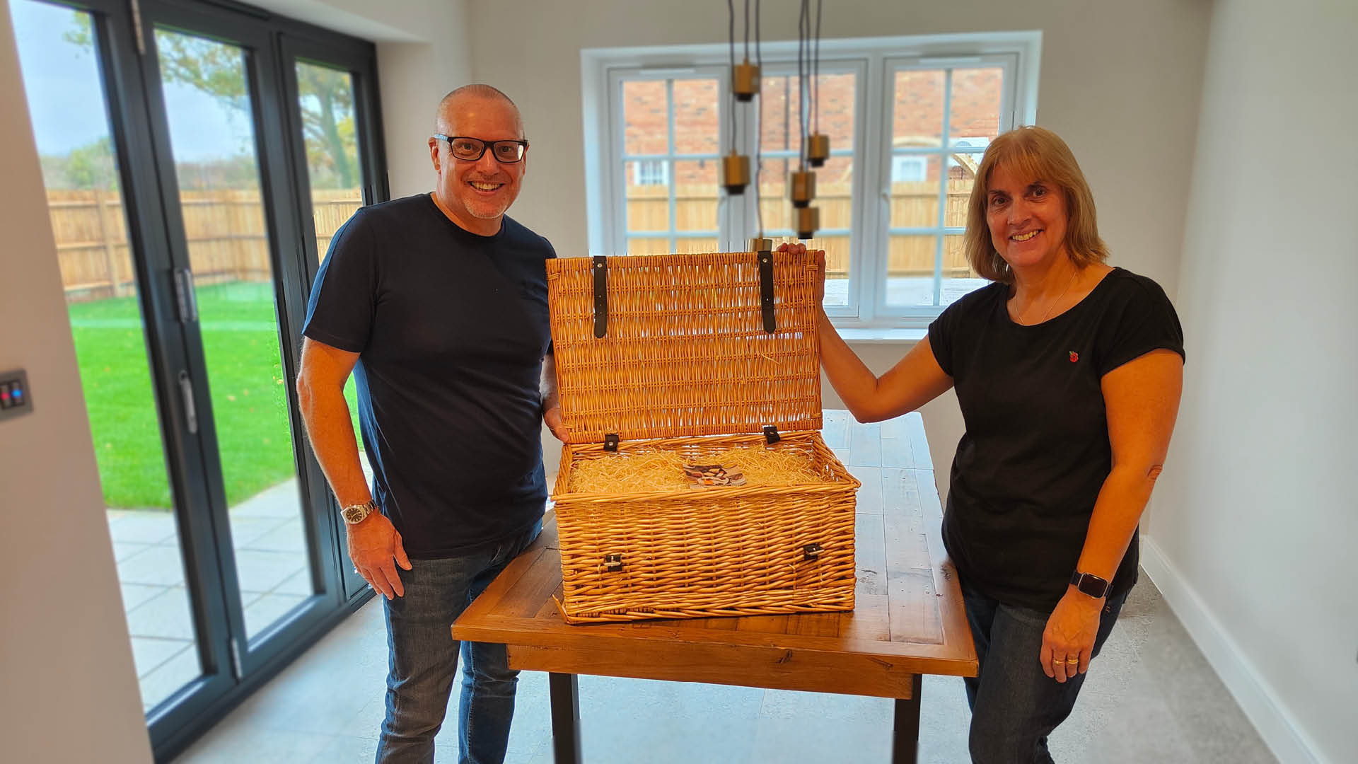 A man and woman standing either side of a wicker hamper in their new build dining room