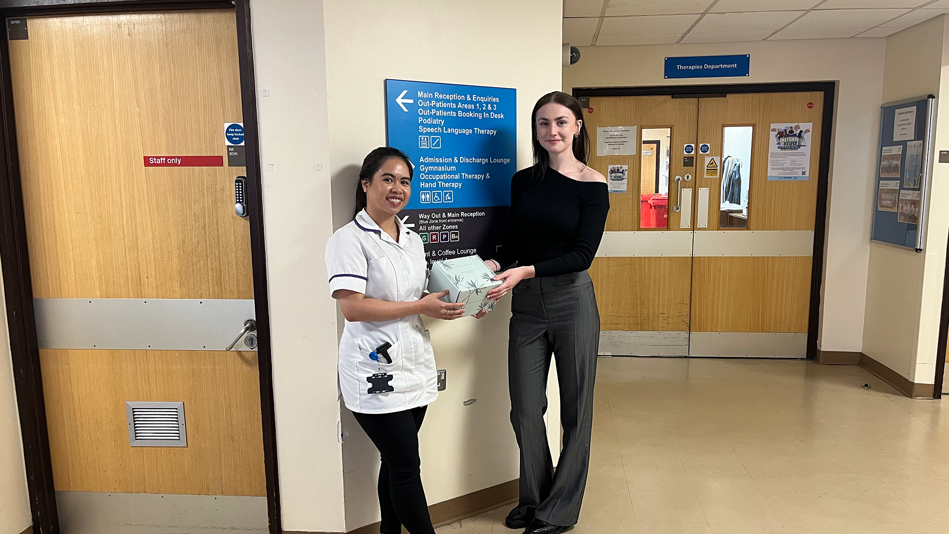 Nurse and Clarendon employee at Medway Maritime hospital stands in front of a sign holding a hamper that has been gifted