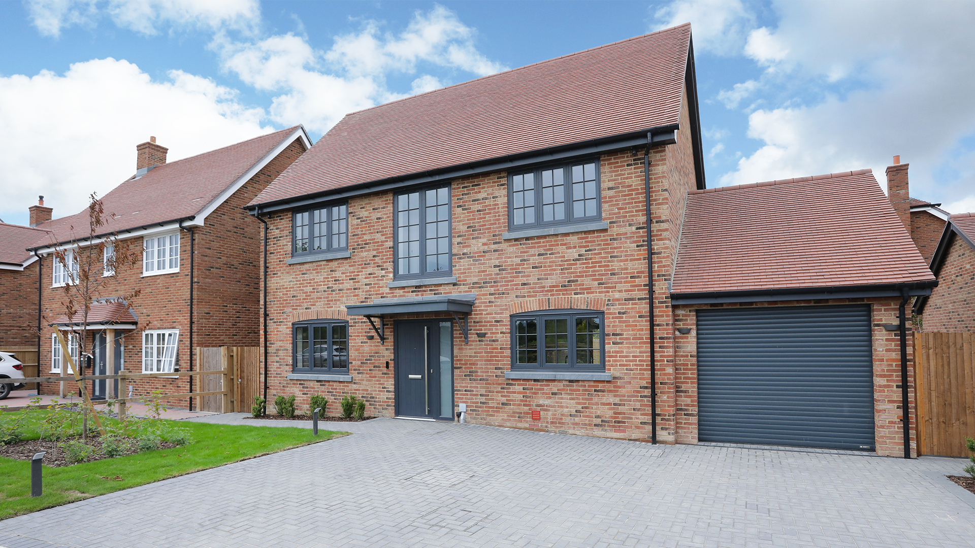 Detached house with red bricks, grey windows and garage door and block pave drive.