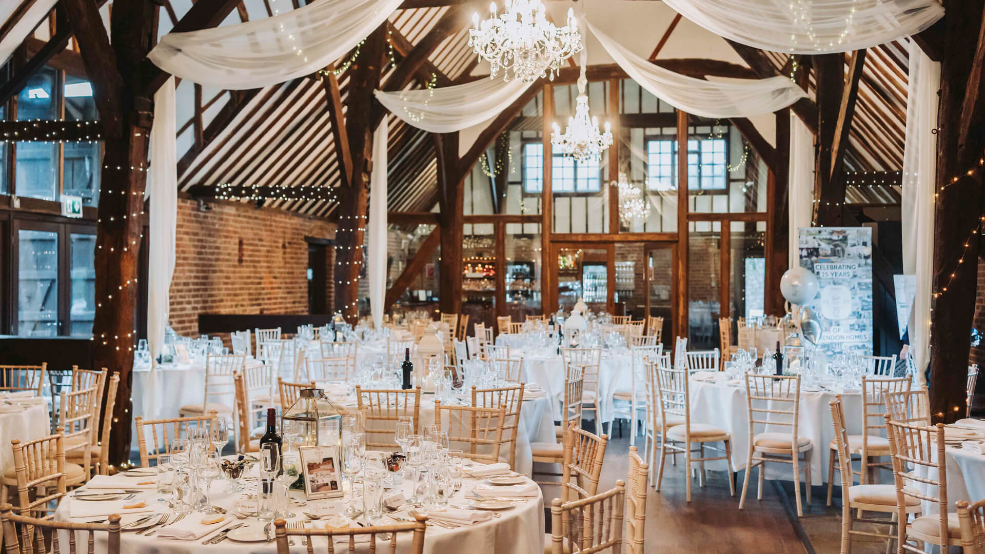 dinner tables set up for an event in a barn with chandeliers hanging from the ceiling