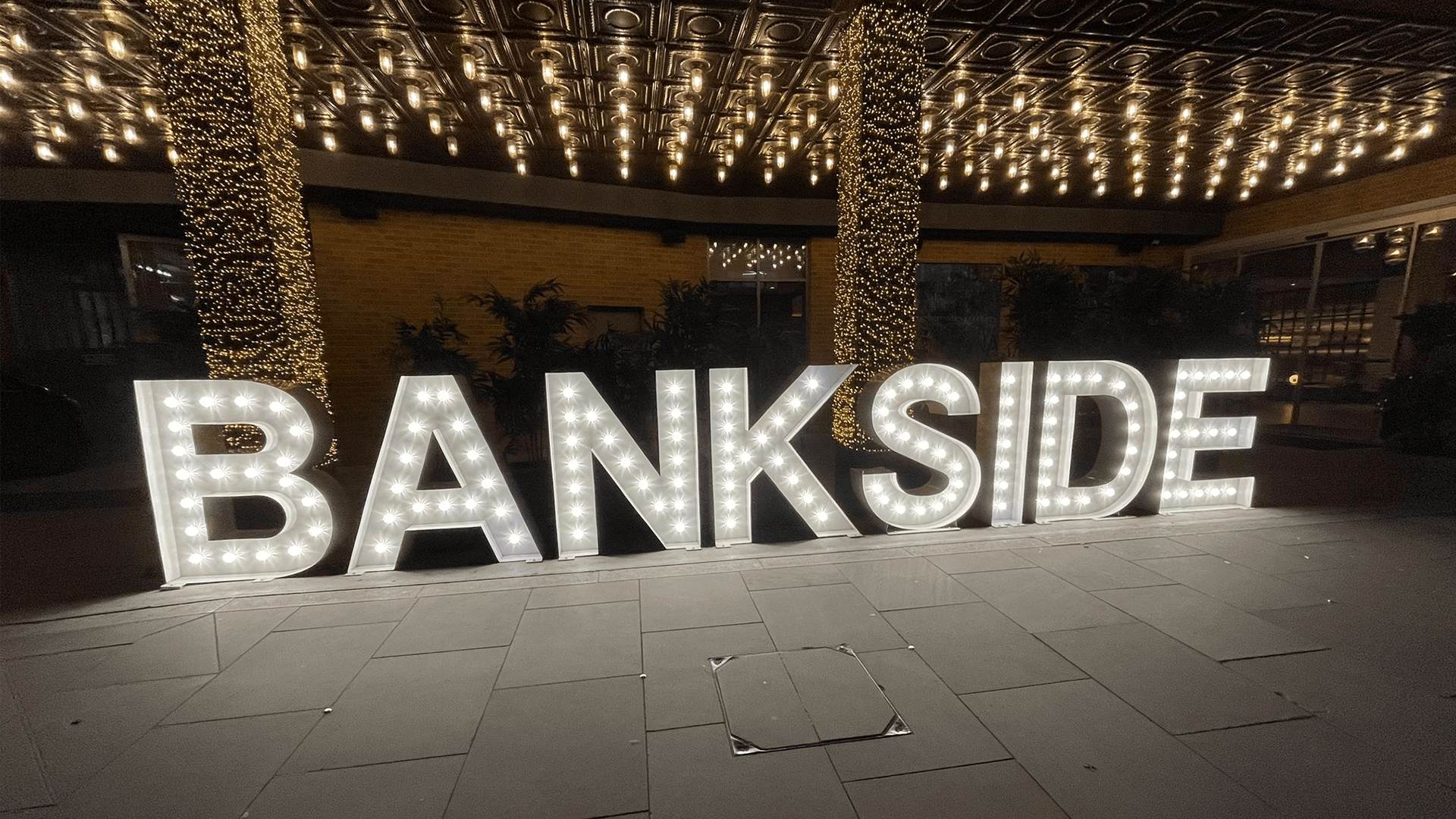 Light up letters outside a building with fairy light in the background