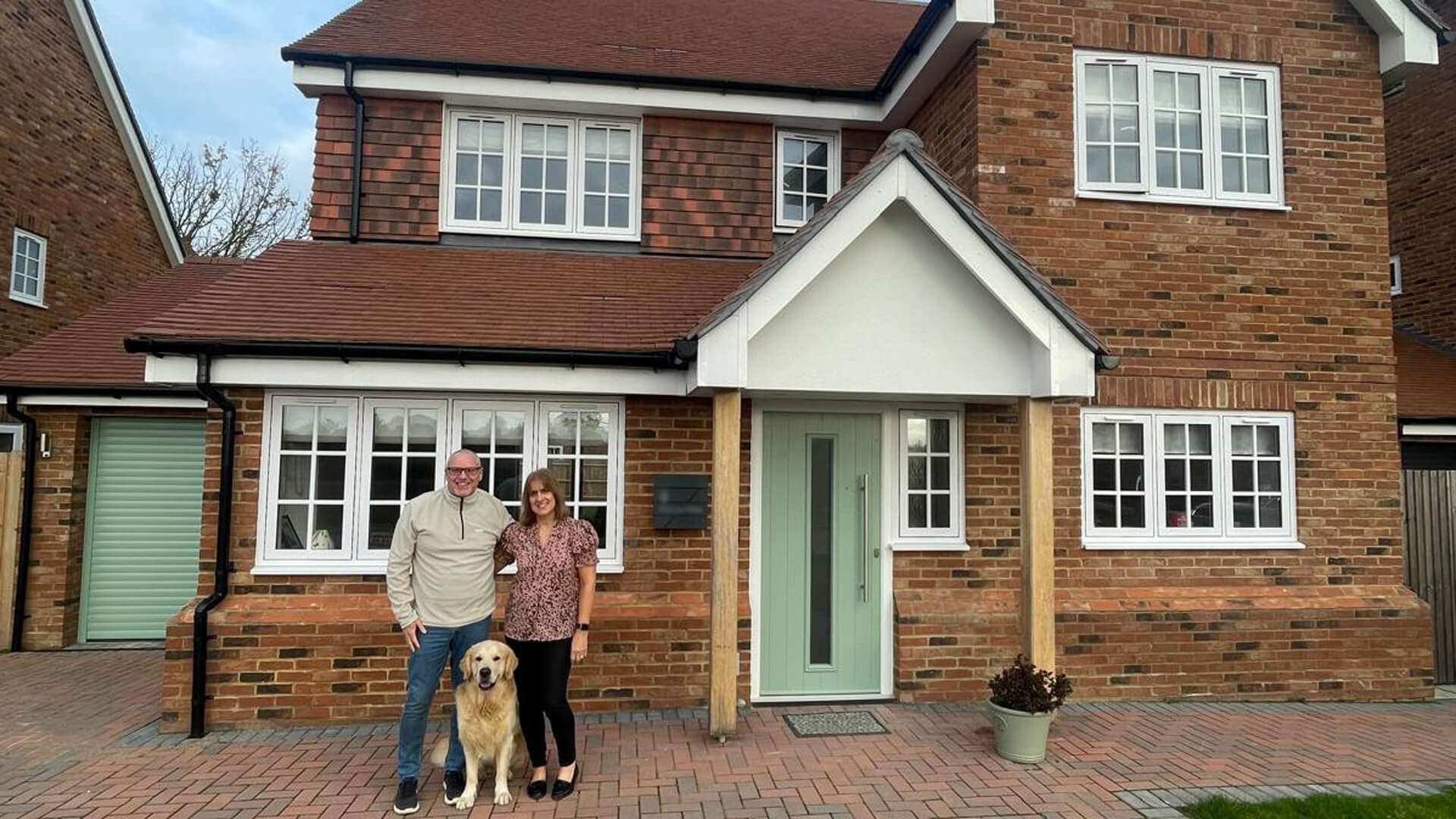 A man and woman with their dog posing for a photo outside their house with a mint green front door and garage