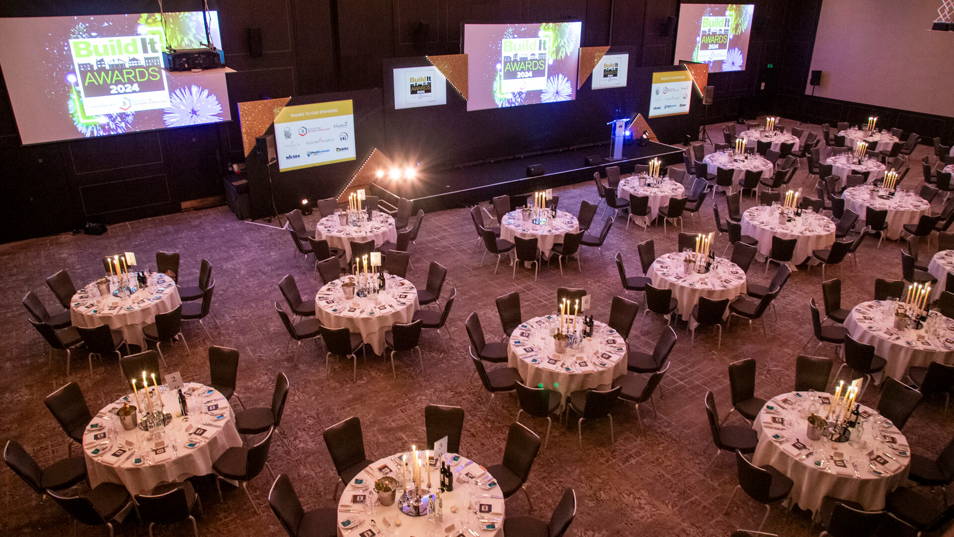 A stage surrounded by round white cloth dining tables with candelabras in the middle of each table