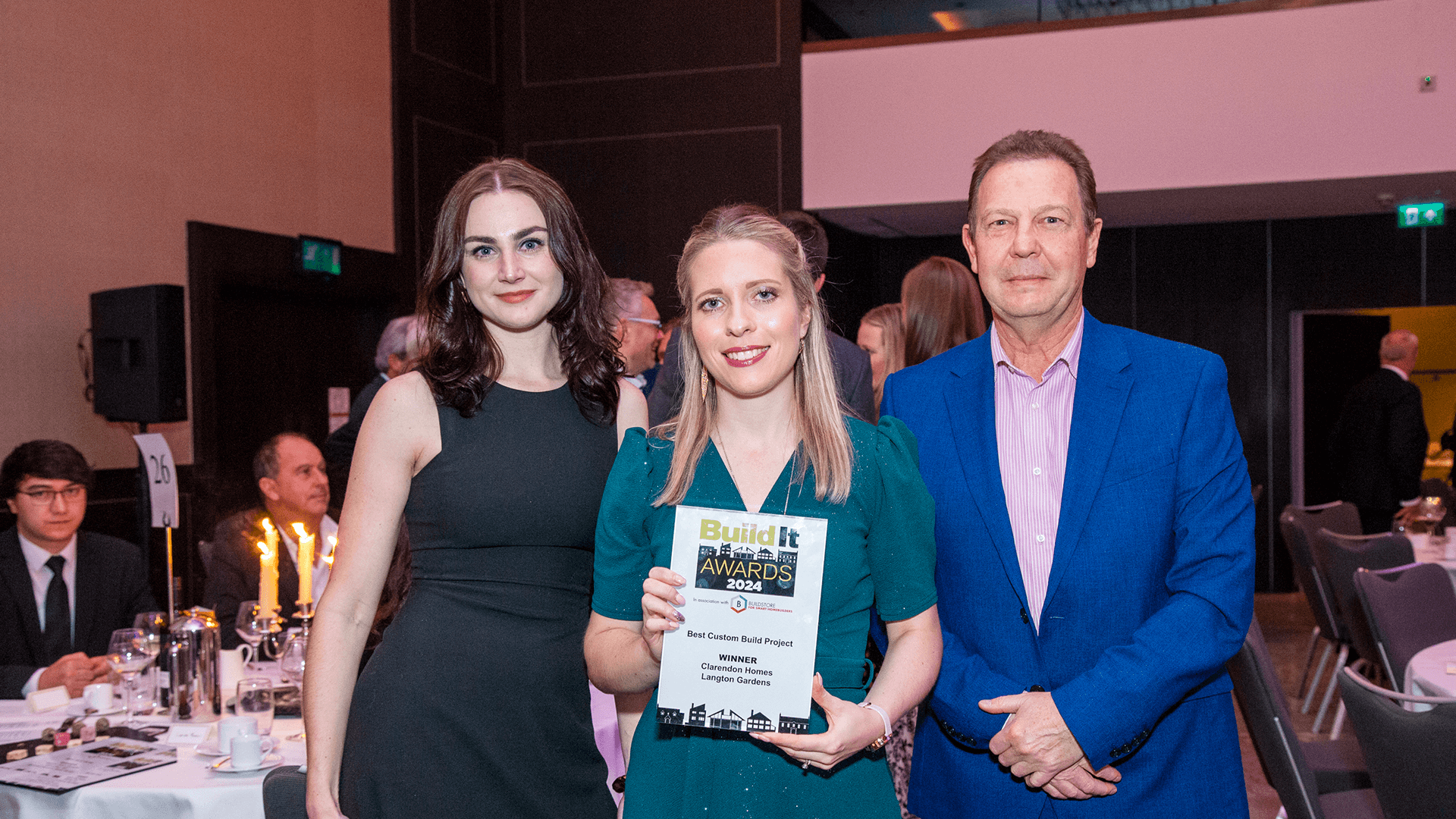 Two women and one man wearing forma outfits, holding a glass award plaque