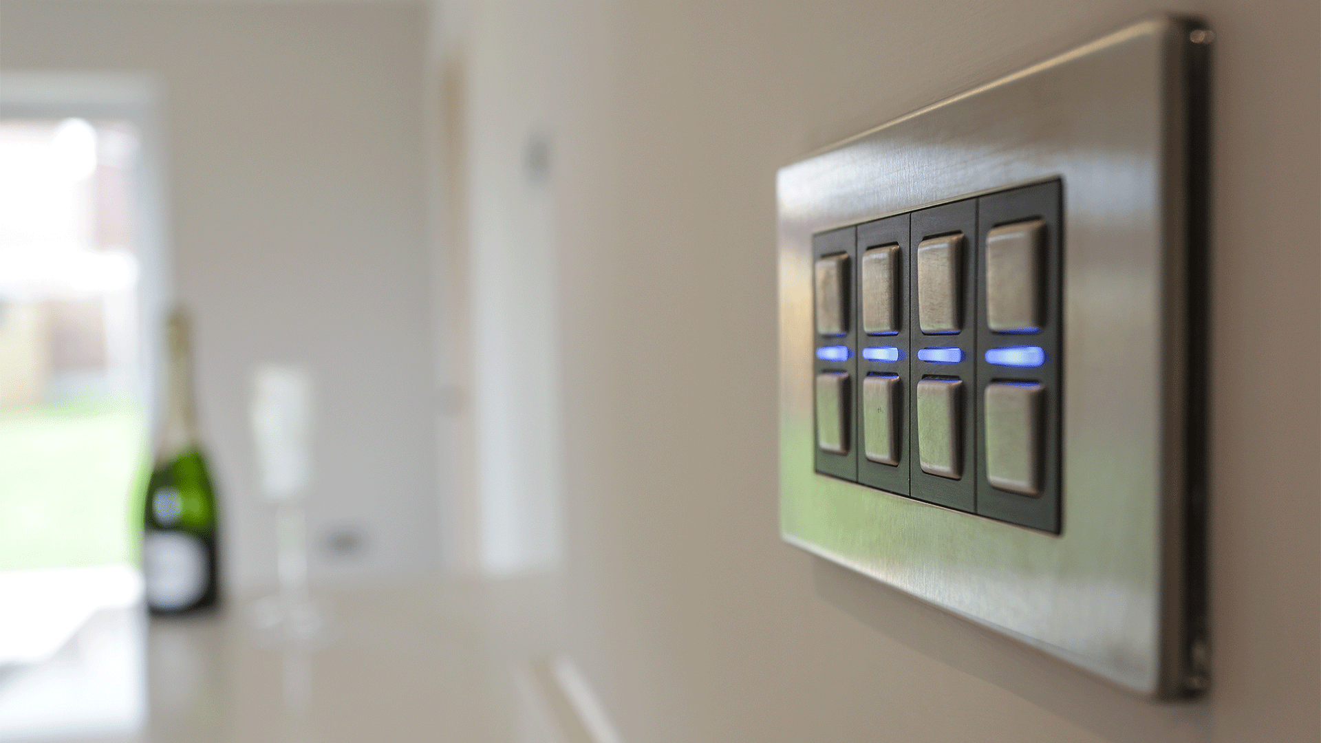 Close up of a smart light switch in chrome with a blurred champagne bottle in the background