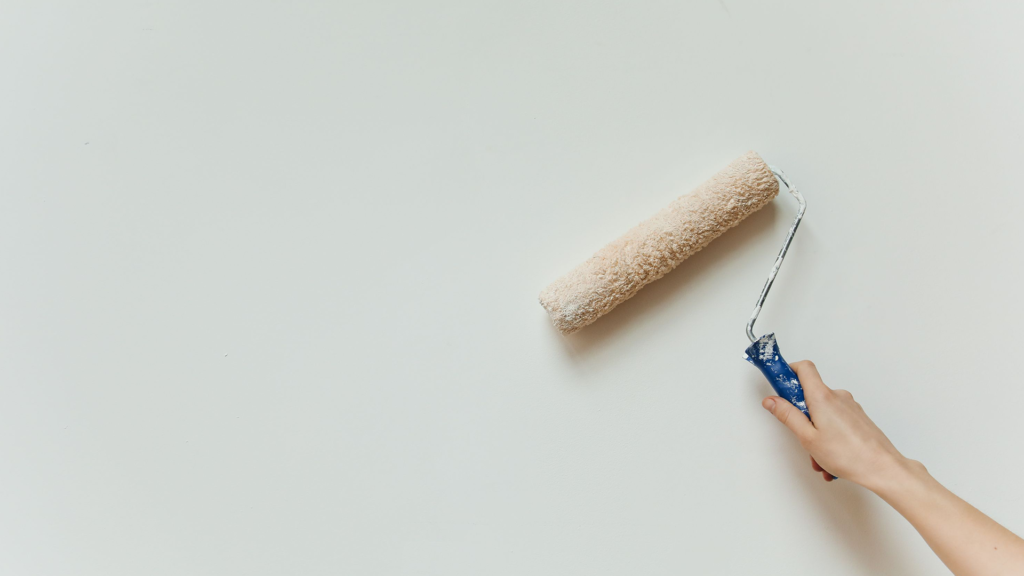 A white wall with someone rolling a paint roller over it as a small finishing touch for snagging process. 