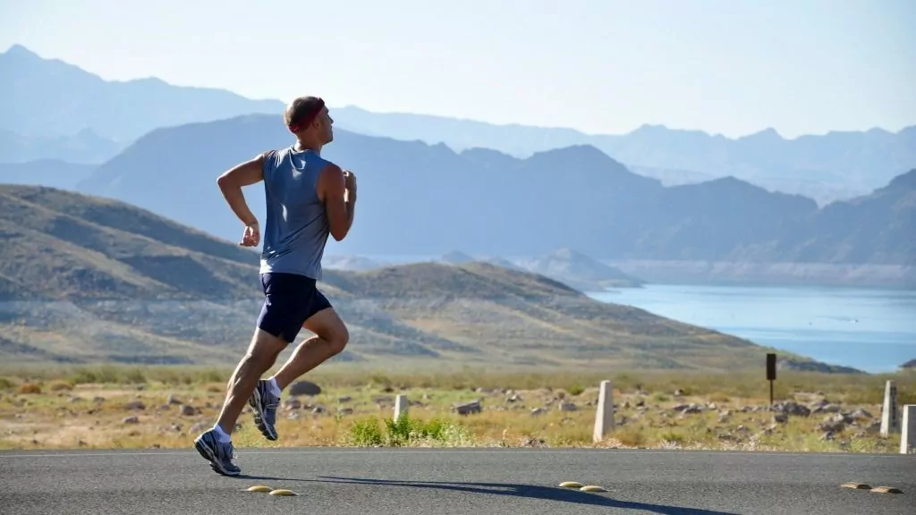 Man running on a road with hill areas behind him